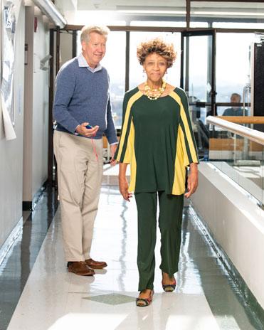 A woman walking down a hallway while a scientist times her progress